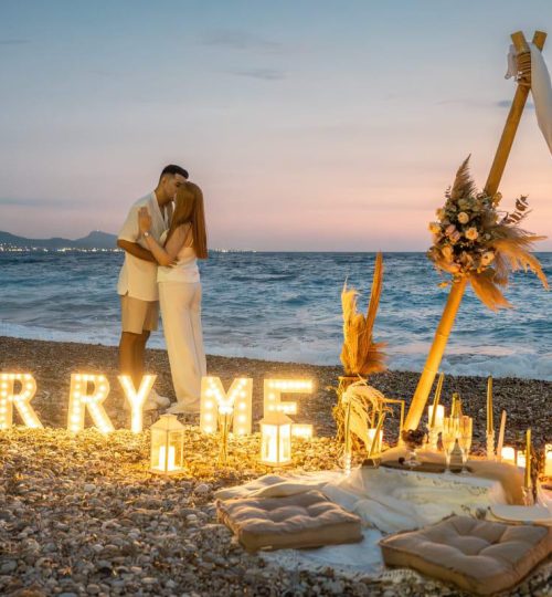 Night beach proposal with illuminated “Marry Me” sign and candles